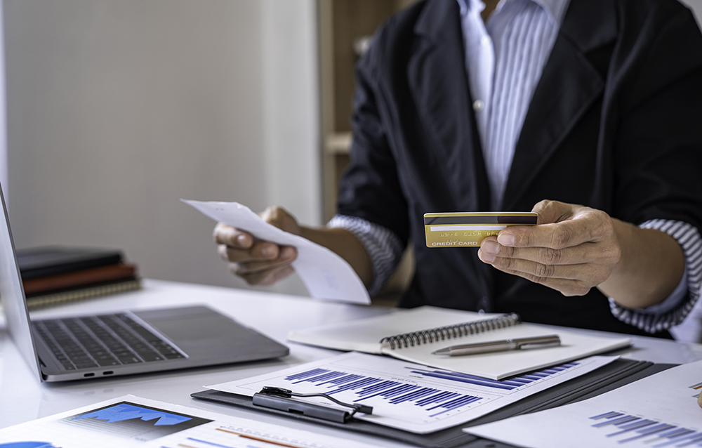Business professional analyzing financial charts while using a credit card.
