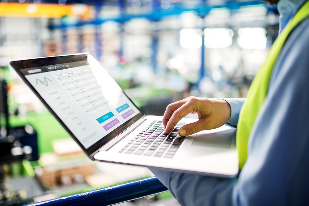 A man uses a laptop to monitor and manage a production system in a factory environment.